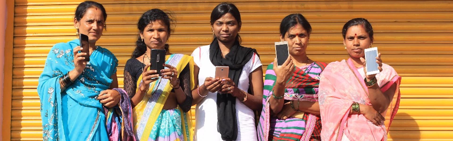 Women workers with Haqdarshak hold up their smartphones.