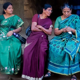 Three Indian women in beautiful saris sit together and one tries to see what another is doing on her cell phone