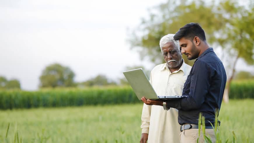Indian farmer talking with man holding computer