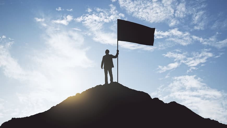 businessman with a flag staking a claim on a mountaintop